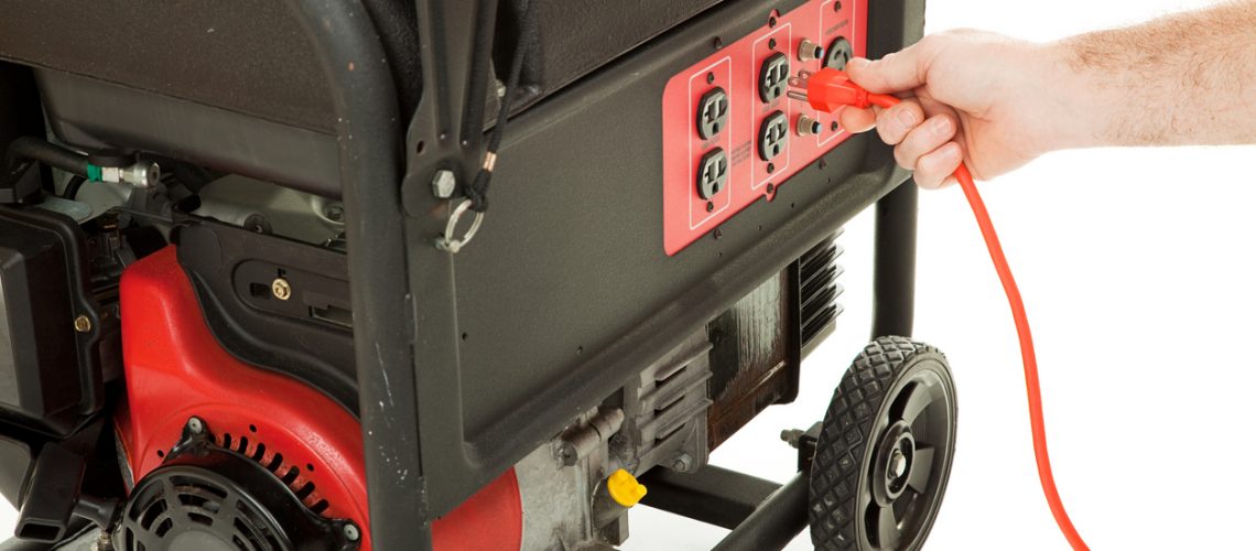 Man's hand plugging an extension cord into an emergency generator.
